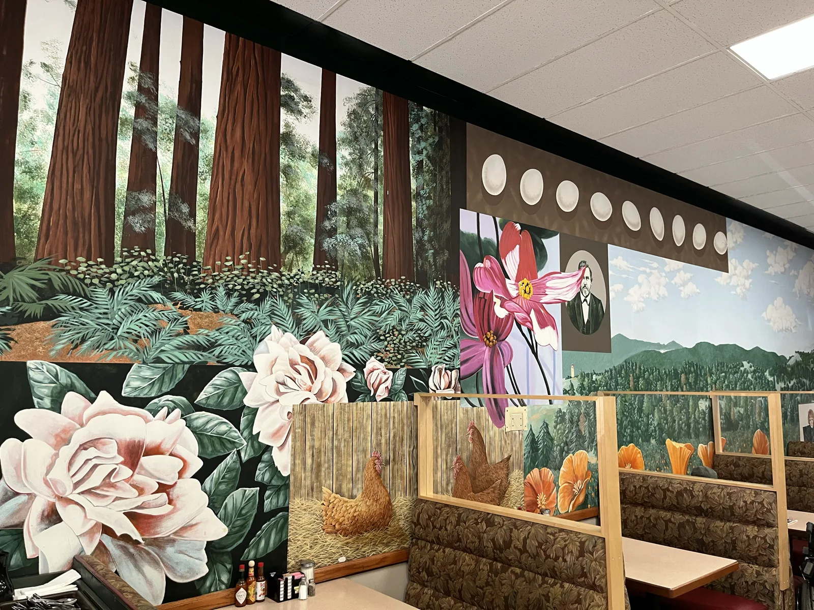 The hand-painted redwood forest and botanical mural inside Breakers Cafe, framing the cozy booth seating.