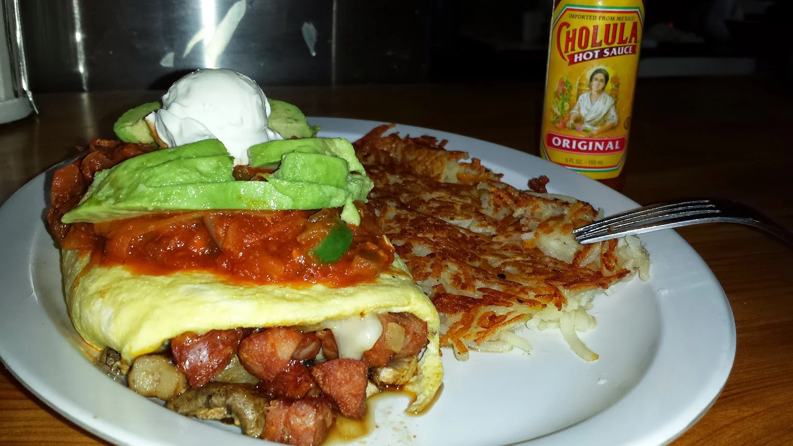 Loaded breakfast omelette with avocado, salsa, and sour cream served with crispy hash browns at Breakers Cafe
